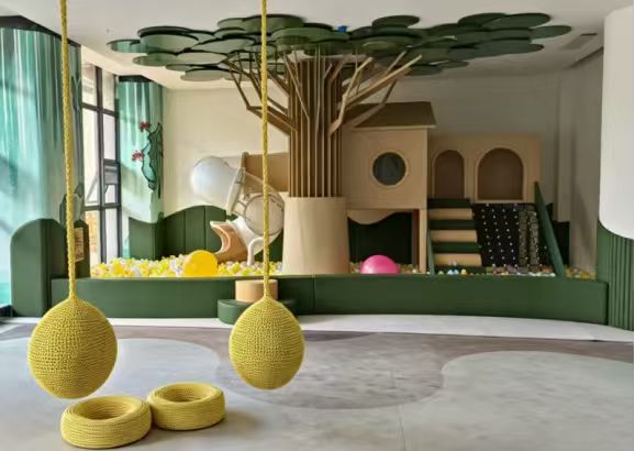 Green tree-themed commercial indoor playground with swings, climbing and soft play zones